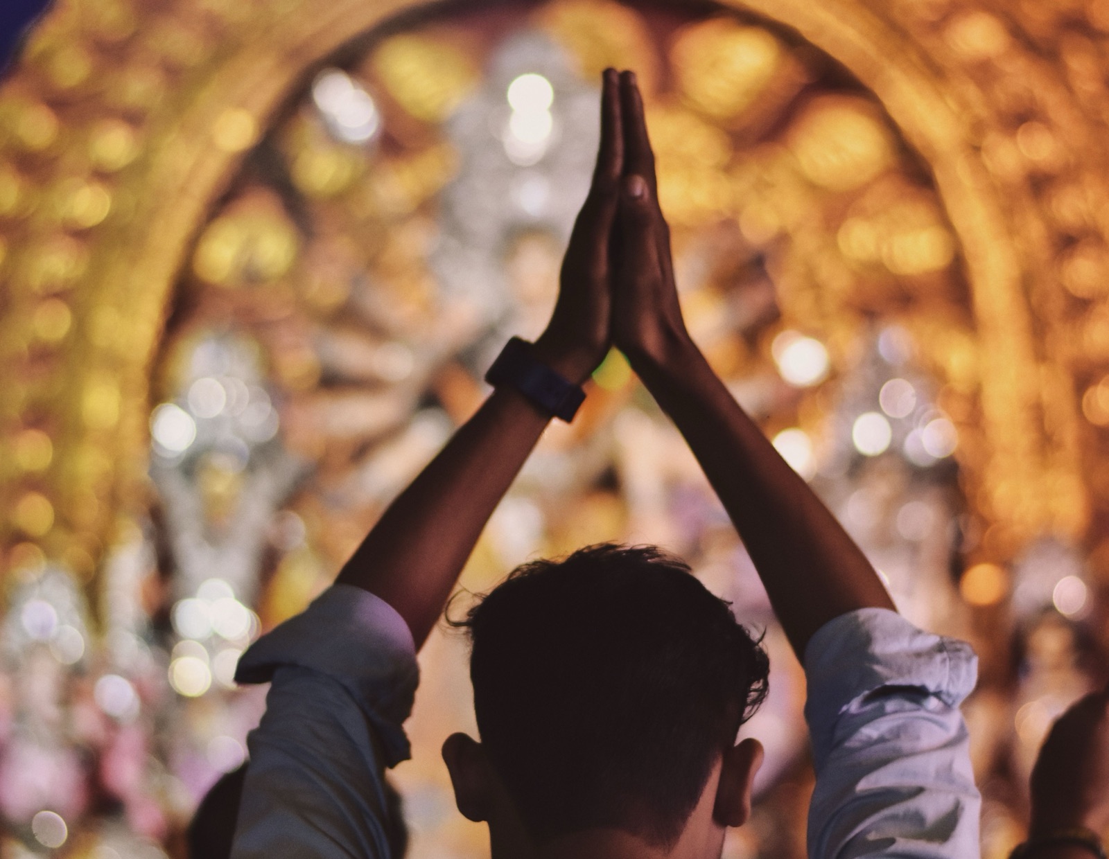 A devotee stands with hands folded in prayer before a golden, garlanded shrine